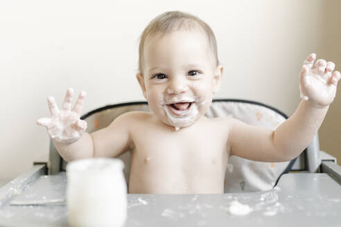 Kleiner Babyjunge isst Joghurt im Hochstuhl zu Hause - JCZF00164