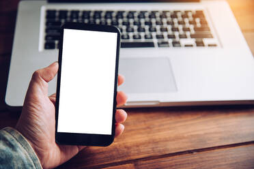 Cropped Hand Of Man Using Smart Phone By Laptop On Table - EYF07521