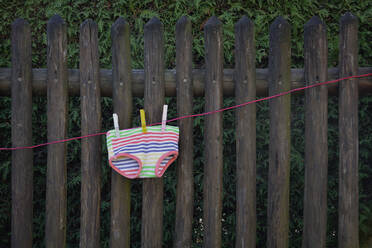 Colorful underpants drying on clothesline in front of wooden fence - AXF00850