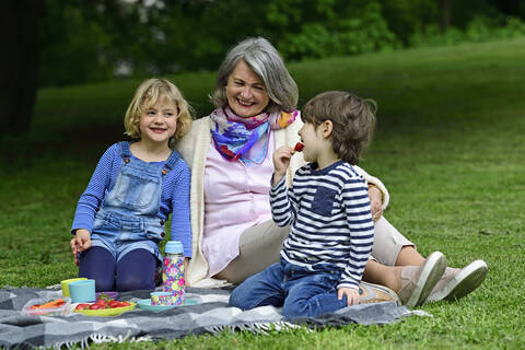 Glückliche Großmutter genießt Picknick mit Enkelkindern im Park, lizenzfreies Stockfoto