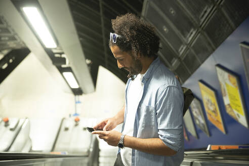 Mann steht auf Rolltreppe und schaut auf sein Handy, London, UK - PMF01114