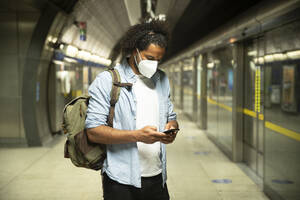 Young man wearing protective mask standing at underground station platform, London, UK - PMF01115