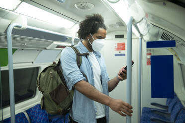Man wearing protective mask standing in underground train looking at cell phone, London, UK - PMF01116