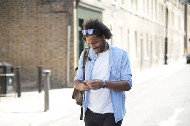 Junger Mann mit Rucksack steht auf der Straße und schaut auf sein Handy, London, UK - PMF01120