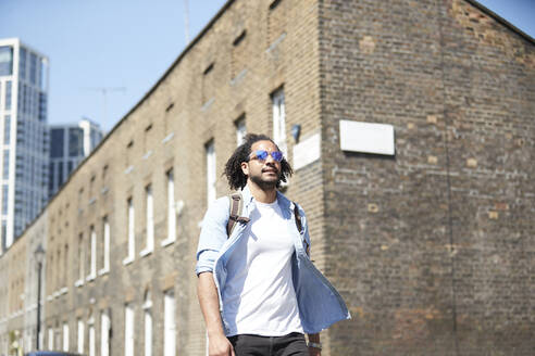 Porträt eines jungen Mannes mit Rucksack und Sonnenbrille auf einer Wohnstraße, London, UK - PMF01122