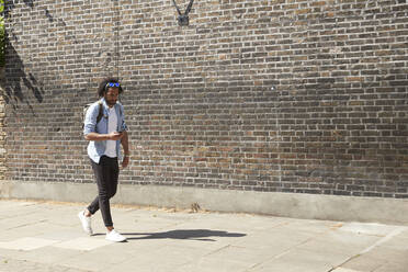 Young man walking on pavement looking at mobile phone, London, UK - PMF01123