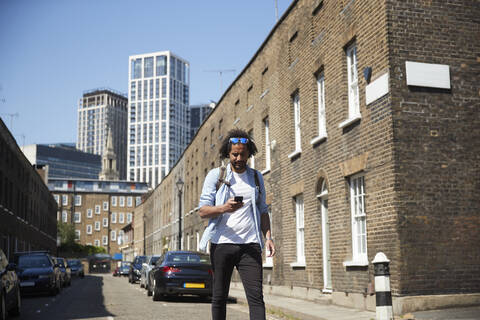 Young man walking on residential street looking at mobile phone, London, UK stock photo