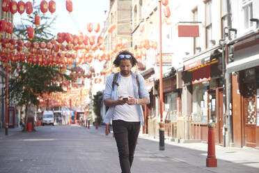 Junger Mann geht auf der Straße und schaut auf sein Smartphone, Chinatown, London, UK - PMF01126