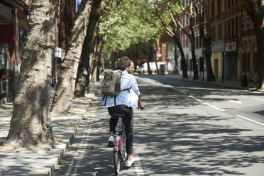 Back view of young man riding rental bike on bicycle lane, London, UK - PMF01136