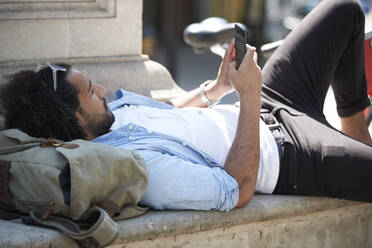 Junger Mann entspannt sich in der Stadt und schaut auf sein Handy, London, UK - PMF01141