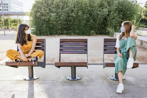 Two friends wearing protective masks meeting outdoors during Corona crisis and keeping distance - TCEF00799