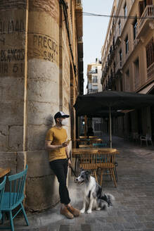 Man wearing protective mask waiting with his dog in the city - AGGF00087