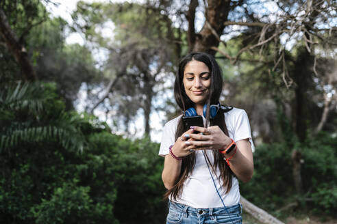 Frau mit Headset und Smartphone im Wald - EGAF00273