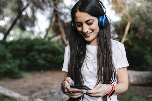 Frau mit Headset und Smartphone im Wald - EGAF00274