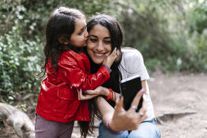 Tochter küsst ihre Mutter, während sie ein Selfie im Wald macht - EGAF00276
