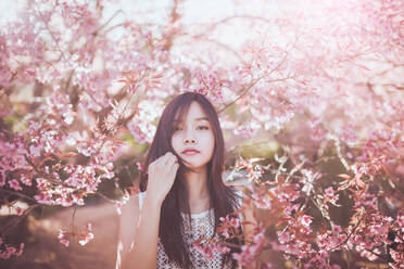 Junge Frau stehend vor Kirschblüten im Park - EYF07649