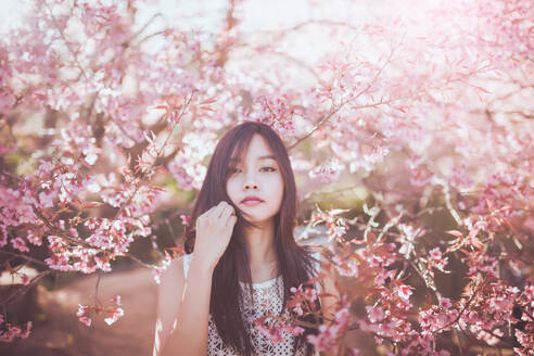 Junge Frau stehend vor Kirschblüten im Park - EYF07649