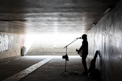 Silhouette des Straßenmusikers, der Gitarre spielt, während er in der U-Bahn singt - EYF07686