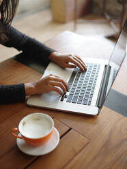 Cropped Hand der Frau mit Laptop mit Kaffee auf dem Tisch - EYF07767