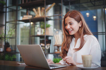 Geschäftsfrau, die einen Laptop benutzt, während sie am Tisch im Cafe sitzt - EYF07769