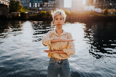 Porträt der jungen Frau Gesturing Equal Zeichen, während stehend gegen See in der Stadt - EYF07825