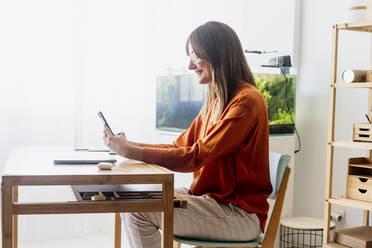 Female freelancer working at home sitting at desk using smartphone - ERRF04010