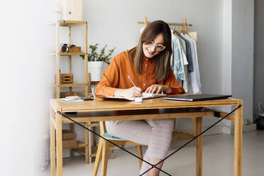 Weibliche Modedesignerin, die zu Hause am Schreibtisch sitzt und Notizen macht - ERRF04014