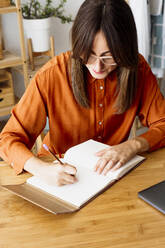 Female freelancer working at home sitting at desk taking notes - ERRF04017