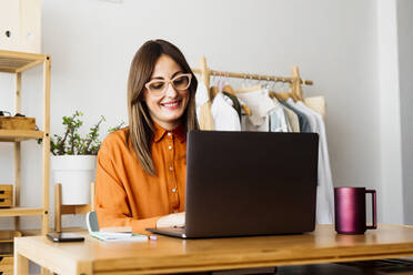 Modedesignerin arbeitet zu Hause am Schreibtisch mit Laptop - ERRF04023