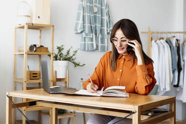 Weibliche Modedesignerin, die zu Hause am Schreibtisch sitzt und Notizen macht - ERRF04027