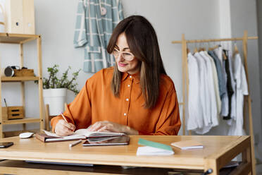 Weibliche Modedesignerin, die zu Hause am Schreibtisch sitzt und Notizen macht - ERRF04033