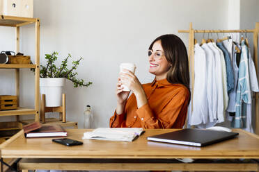 Weibliche Modedesignerin sitzt zu Hause am Schreibtisch und macht eine Kaffeepause - ERRF04040