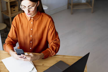 Female freelancer working at home sitting at desk using smartphone - ERRF04042