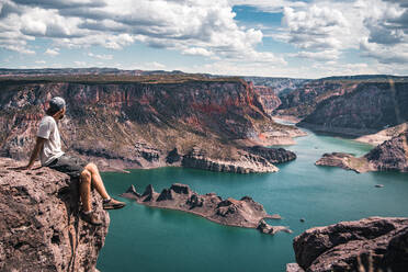 Man Looking At View While Sitting On Cliff Against Mountains And Cloudy Sky - EYF07837