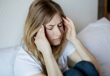 Frau mit Kopfschmerzen auf dem Bett sitzend zu Hause - EYF07896