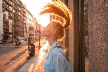 Side View Of Young Woman Tossing Hair While Standing On Sidewalk During Sunset - EYF07956