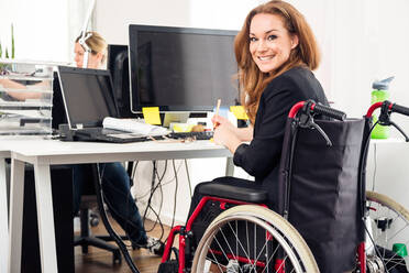 Portrait Of Businesswoman Sitting On Wheelchair At Desk In Office - EYF07959