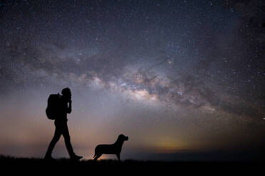 Silhouette Mann geht mit Hund auf Feld gegen Sternfeld - EYF07979