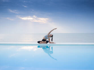 Frau übt Yoga auf Infinity-Pool am Meer gegen bewölkten Himmel - EYF07989