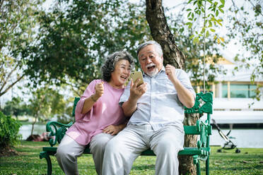 Glückliches älteres Paar mit Smart Phone im Park - EYF07997
