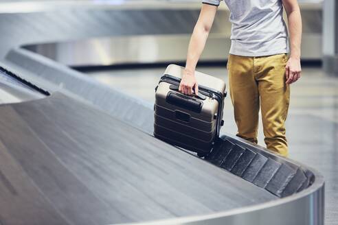 Midsection Of Man Picking Suitcase From Conveyor Belt - EYF08038