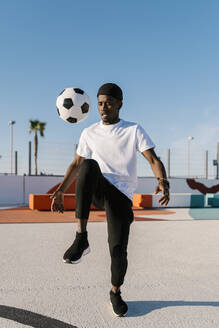 Junger Mann jongliert mit Fußball gegen den klaren Himmel im Hof - EGAF00295