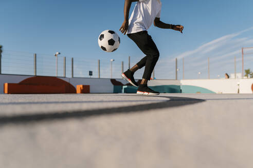 Junger Mann jongliert mit Fußball auf einem Sportplatz gegen den Himmel - EGAF00298