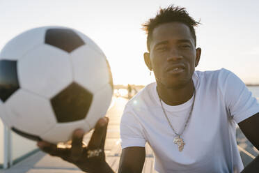 Nahaufnahme eines jungen Mannes, der einen Fußball gegen einen klaren Himmel an einem sonnigen Tag hält - EGAF00306