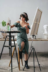 Full Length of Painter Sitting On Stool By Easel At Art Studio - EYF08060