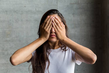 Junge Frau mit Händen, die die Augen bedecken, an der Wand - EYF08074