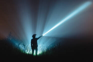 Mann mit beleuchtetem Blitzlicht stehend auf Feld gegen Himmel bei Nacht - EYF08077