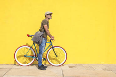 Side View Of Man With Bicycle Standing On Footpath Against Yellow Wall - EYF08090