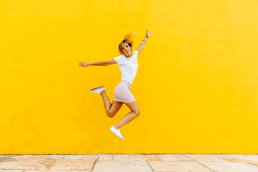 Volle Länge der glücklichen Frau Springen gegen gelbe Wand - EYF08103