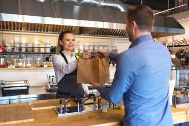 Besitzer gibt Papiertüte zum Kunden im Café stehend - EYF08104